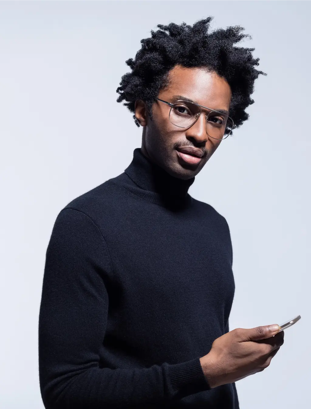 A man wearing glasses and a black turtleneck is holding a cell phone.