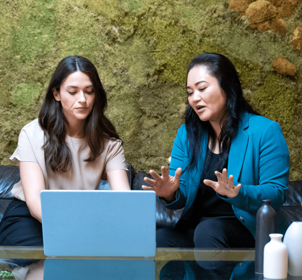 Image de deux femmes assises devant un ordinateur portable en train de discuter.