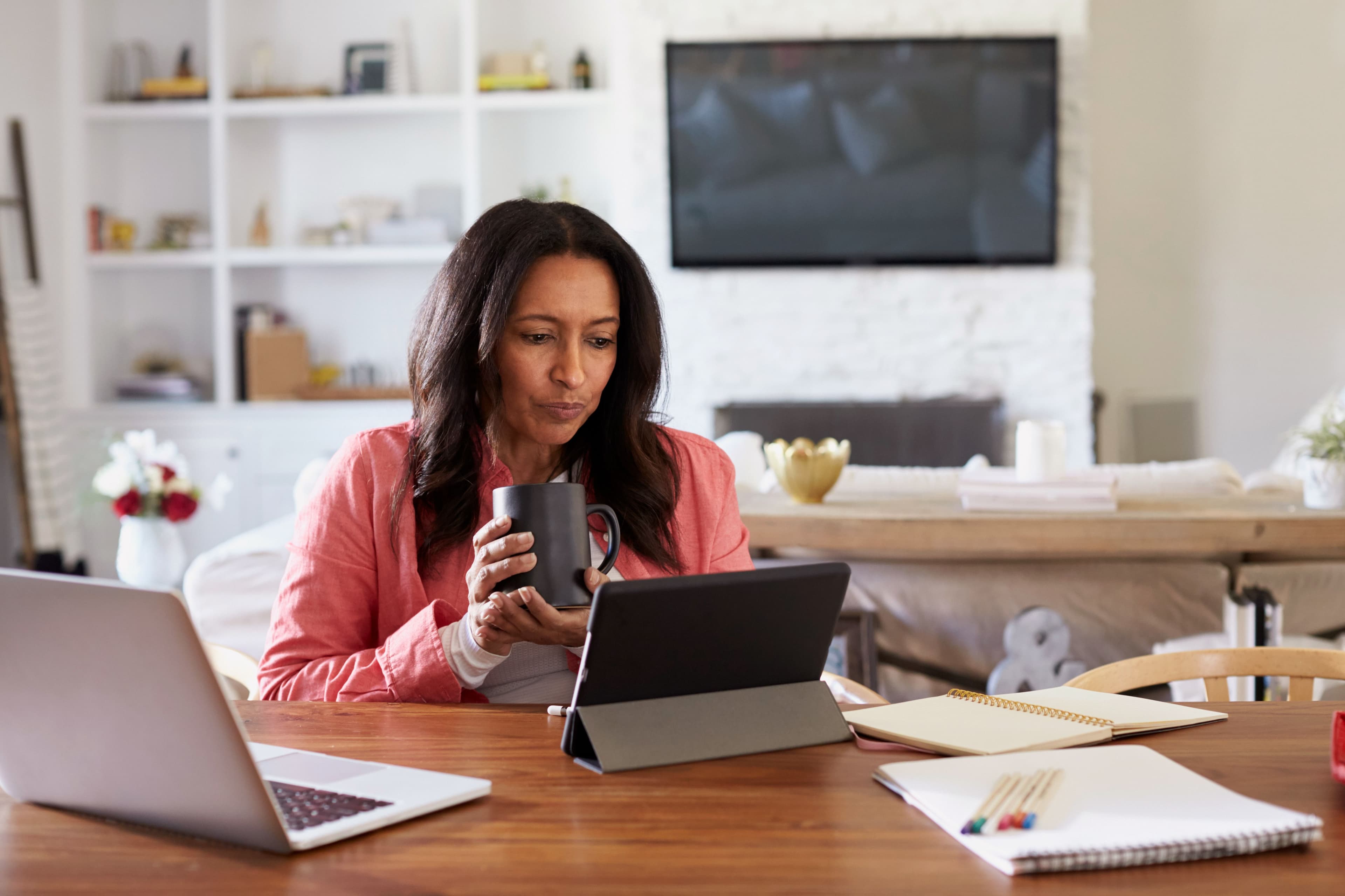 Women holding a cup of coffee while looking at tablet on desk.