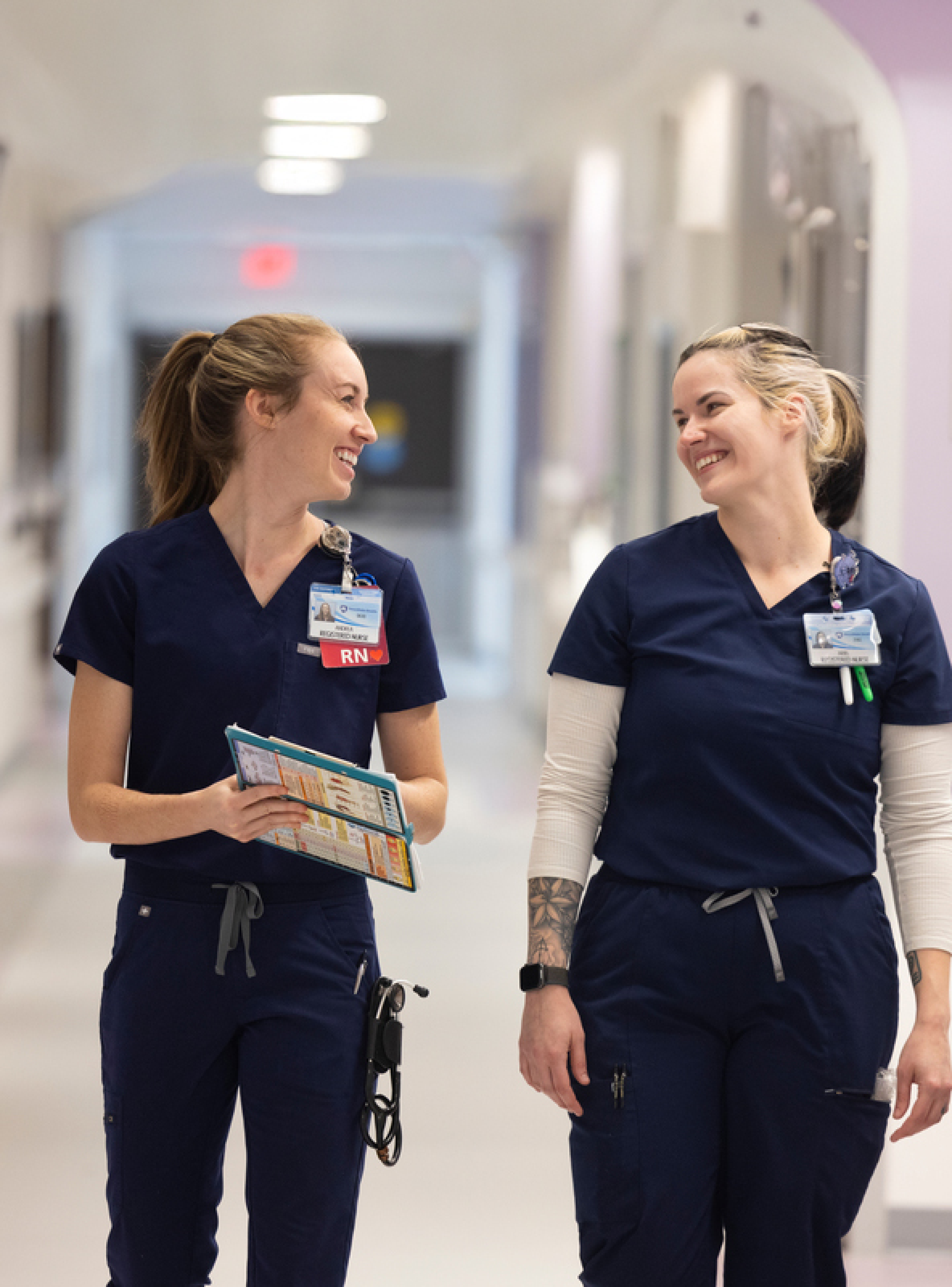Image of two healthcare workers walking down the hallway together during their shift at a healthcare facility.