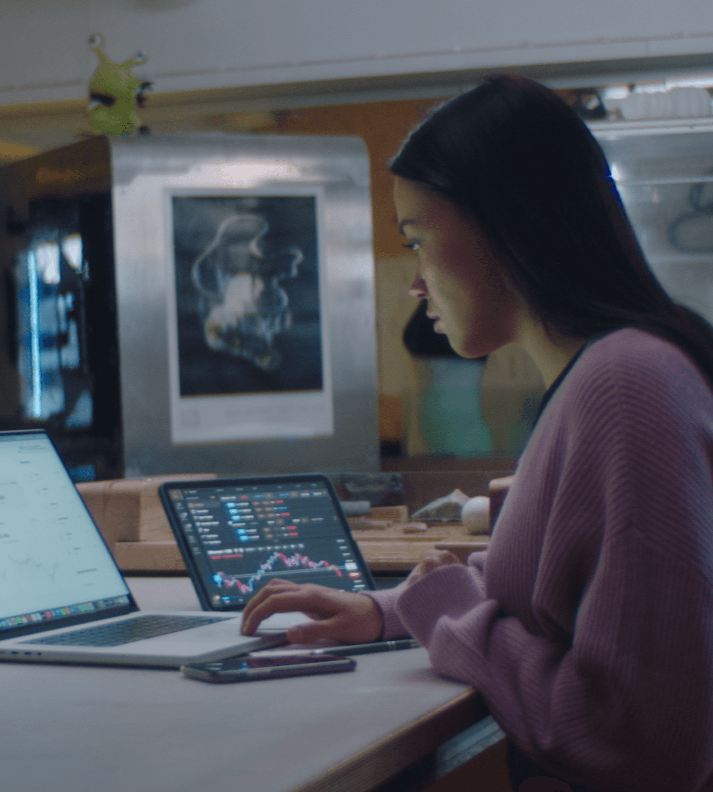 Image of a woman working at a desk in an office with a laptop and a tablet.