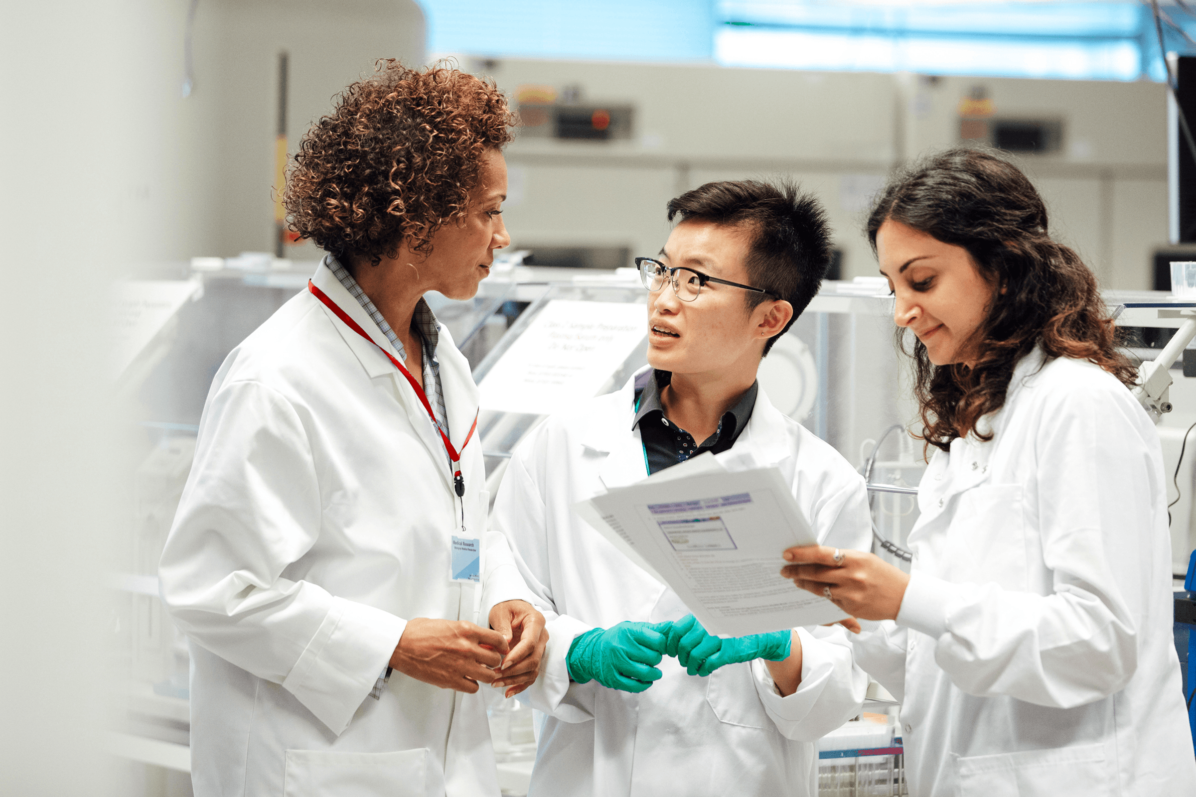 Three scientists in lab coats discussing documents in a lab.