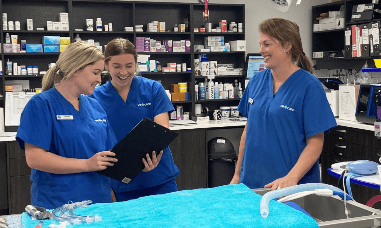 3 Vetcare employees at their office smiling and viewing a document on a clip board.